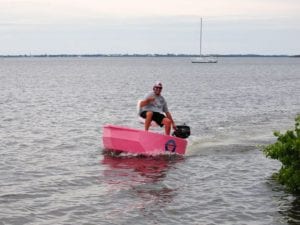 A pink round boat going full speed with a gas engine.
