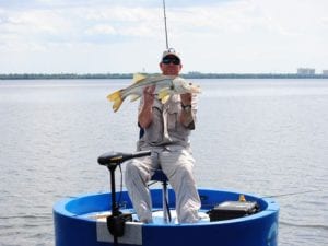 A fisherman holding a snook he just caught from a blue round boat